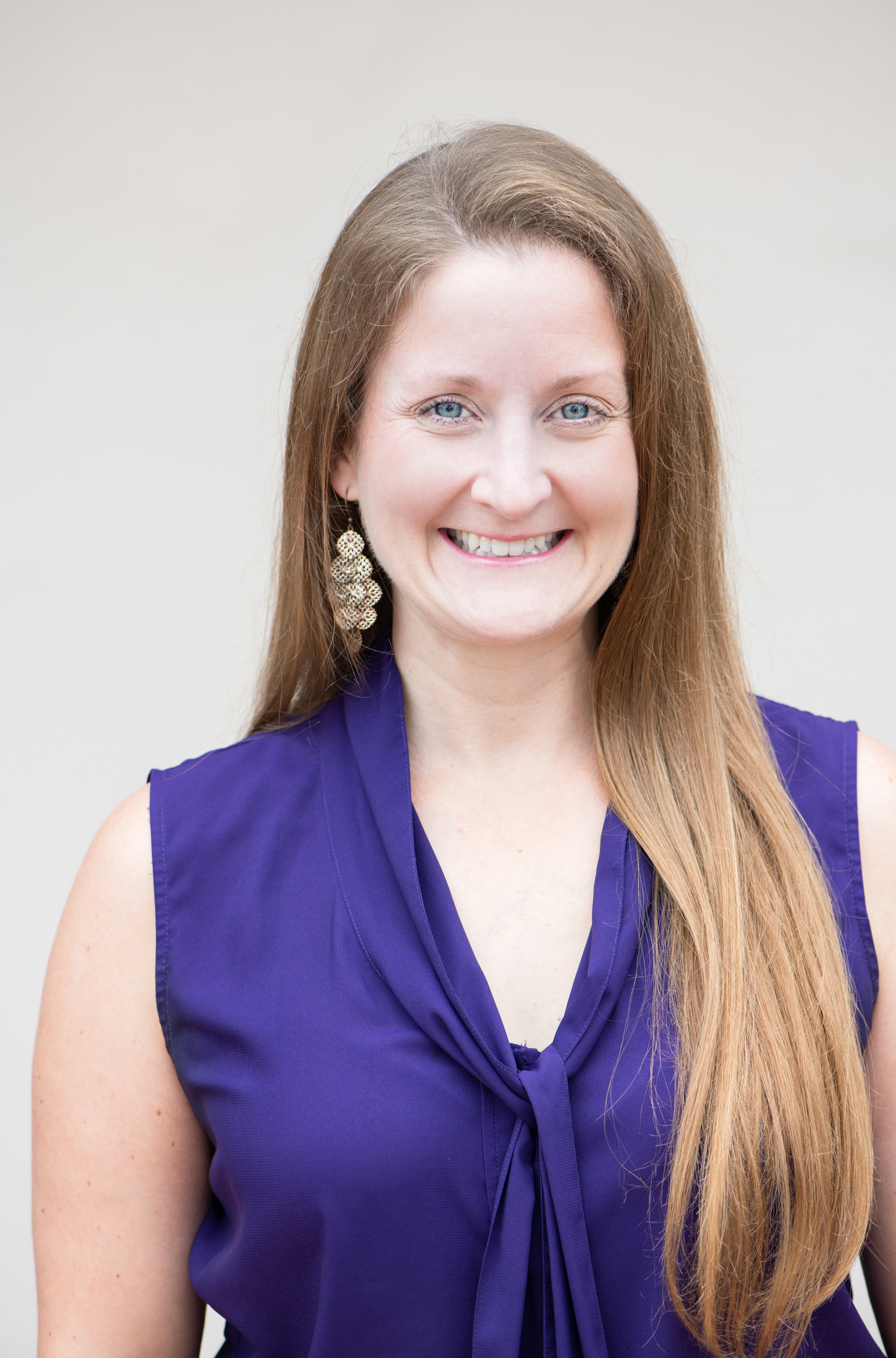 a smiling headshot of jessica with a purple shirt, long hair over one shoulder and gold earrings